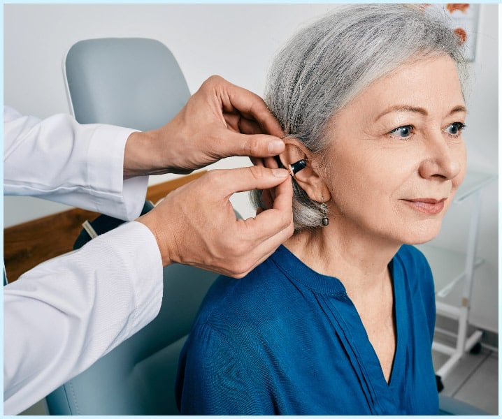 Woman getting her hearing aids fitted to her ears by her audiologist