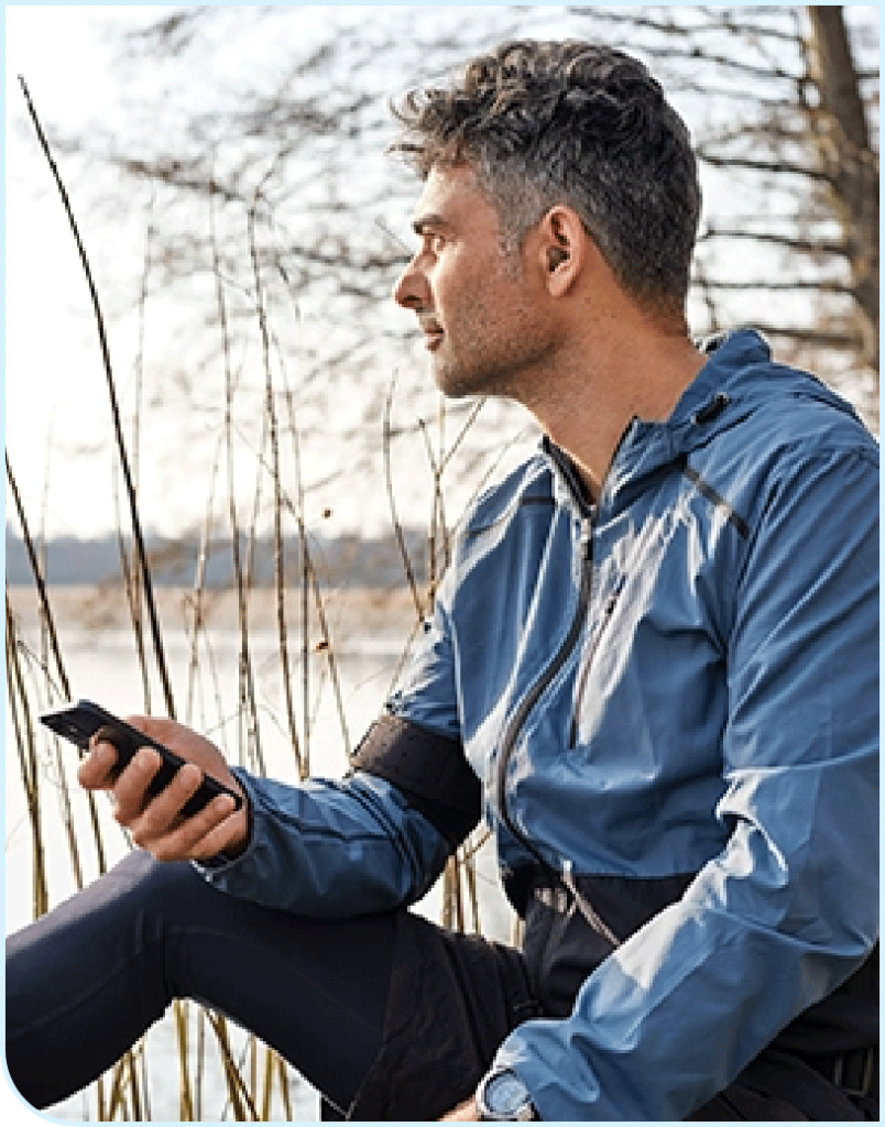 Man sitting outside with his Oticon hearing aids connected to his smart phone
